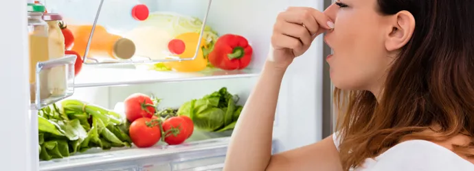 Femme qui se bouche le nez devant un frigo ouvert rempli d'aliments variés.