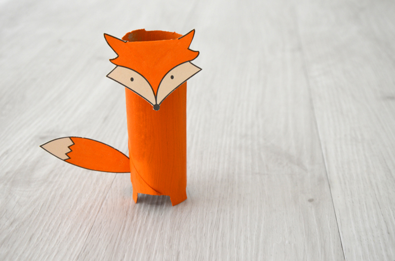 Un animal en carton en forme de renard fait d'un tube d'essuie-tout orange avec un visage et une queue en papier.