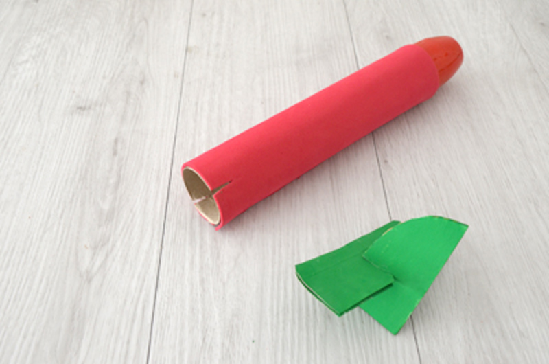 Une gouverne de direction verte d'un avion en carton et un fuselage rouge fait d'un tube en carton.