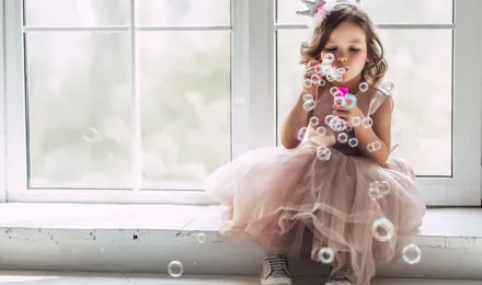 Une petite fille en costume de princesse rose fait des bulles