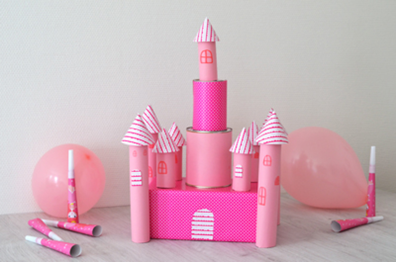 Un château de princesse en carton fini, avec des tours cylindriques, des toits coniques et des ballons de chaque côté.