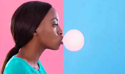 Vrouw blaast een kauwgombel tegen een roze en blauwe achtergrond