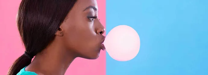 Vrouw blaast een kauwgombel tegen een roze en blauwe achtergrond