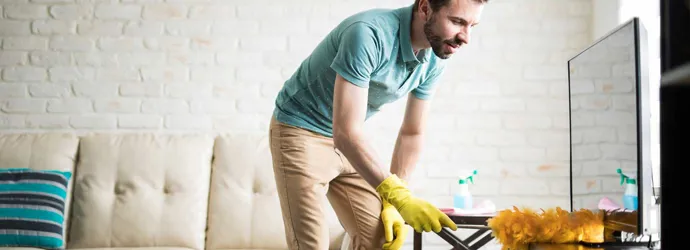 Un homme dépoussière sa maison avec un chiffon