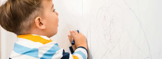 Un bébé dessine sur un papier peint propre avec des crayons