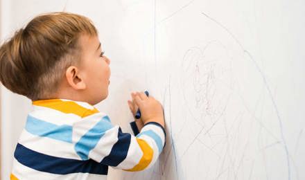 Un bébé dessine sur un papier peint propre avec des crayons