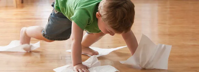 Un enfant nettoie le sol avec des essuie-tout