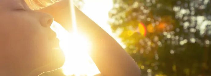 Un enfant est dehors sous le soleil et pose une bouteille d'eau sur son front pour se rafraîchir.