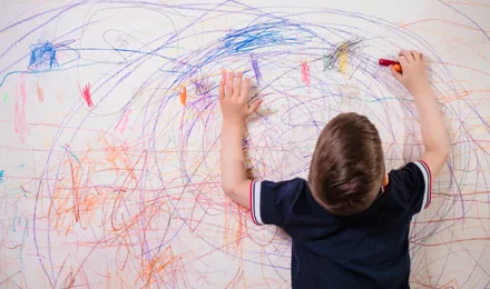 Enfant gribouillant sur un mur avec des crayons colorés