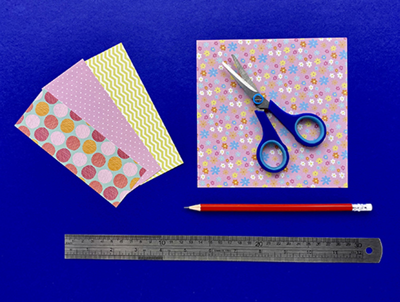 Bandes de tissu adhésif colorées, une paire de ciseaux, un crayon et une règle sur un fond bleu.